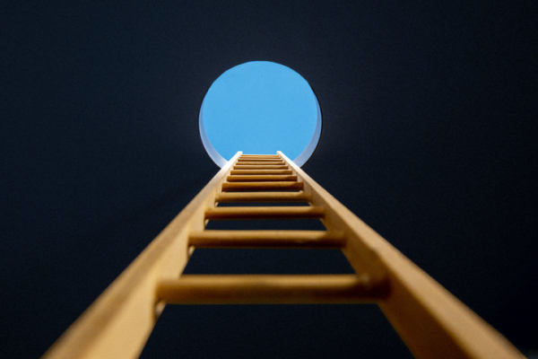 A wooden ladder with rungs heading upward from a dark place into a circle of blue sky; concept is therapy 